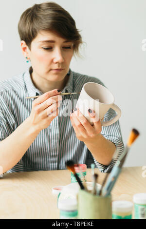 La ceramica donna tiene in mano una tazza di dipingere l'ornamento, di ceramica fatti a mano Foto Stock