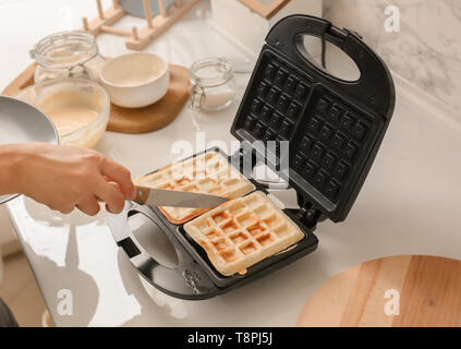 Donna prendendo fette fresco fuori della piastra per i waffle in cucina Foto Stock