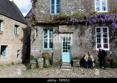 Due turisti senior seduto alla tradizionale casa in pietra con glicine crescente su facciate in conserve di borgo medievale di Locronan in Bretagna, Francia Foto Stock
