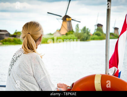 Immagine vista posteriore da una barca di donna che guarda indietro verso mulini a vento in background, reminiscing delle cose nei pasted.canal corsi d'acqua, Olanda, Europa. Foto Stock