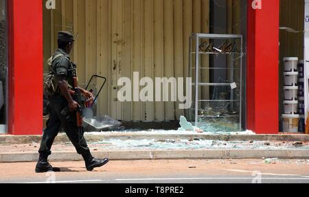 Colombo, Sri Lanka. 14 Maggio, 2019. Un membro delle forze di sicurezza passeggiate passato una casa danneggiata in Nord provincia occidentale, Sri Lanka, 14 maggio 2019. Oltre 60 persone sono state arrestate oltre i violenti scontri che è scoppiata in Sri Lanka il lunedì, la polizia ha detto in una dichiarazione martedì. Un locale gruppo radicale, denominato Thawheed nazionale Jammath, è stato accusato per gli attacchi. Credito: Gayan Sameera/Xinhua/Alamy Live News Foto Stock