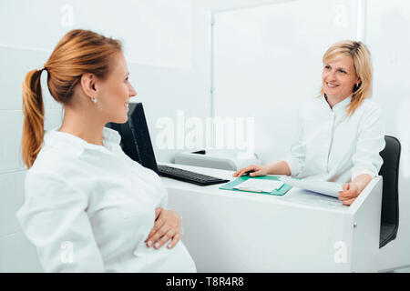 Sorridente ostetrico a parlare con una donna incinta clinica nella sala esame Foto Stock