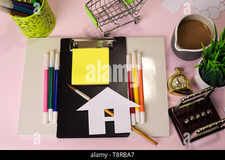 Vista superiore del taglio della carta o del disegno casa su una tabella di colore rosa, preparando a fare i compiti in un blocco appunti. Disegno Scrivania Concept Foto Stock