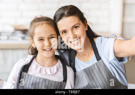 Carino bambina e la sua mamma In grembiuli rendendo Selfie Foto Stock