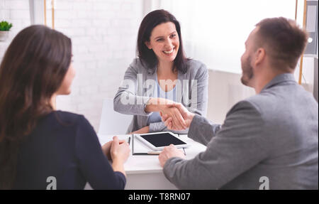 Donna sorridente broker assicurativo e giovane famiglia stringono le mani Foto Stock