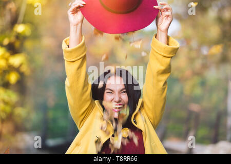 In autunno le foglie che cadono al di fuori di un cappello. Outdoor ritratto di un bel giovane donna gode in autunno park. tramonto, il fuoco selettivo Foto Stock