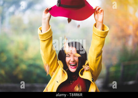 Colorato foglie che cadono da hat caduta su felice giovane donna in foresta, outdoor ritratto, il fuoco selettivo Foto Stock