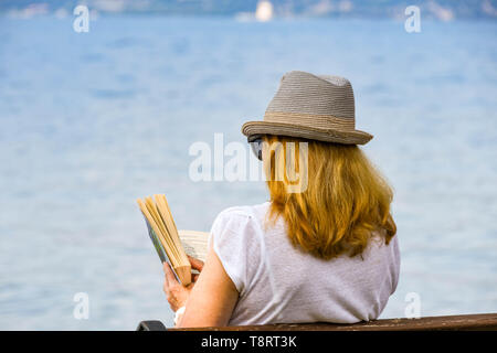 TORRI DEL BENACO SUL LAGO DI GARDA, Italia - Settembre 2018: persona che legge un libro seduta su una panchina in riva al lago, nel comune di Torri del Benaco sul Lago di Garda Foto Stock