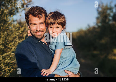 Ritratto di Padre azienda piccola figlia in piedi all'aperto da olivo. Foto Stock