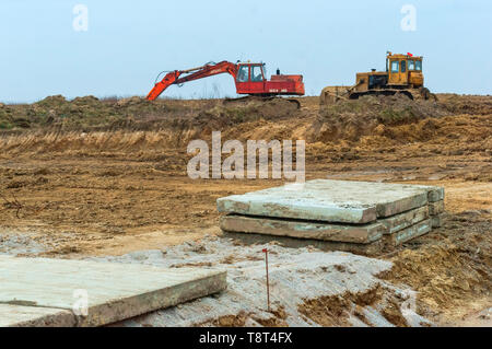 Macchine da costruzione in campo, le lastre di cemento sul terreno e escavatore, la regione di Kaliningrad, Russia, 3 marzo 2019 Foto Stock