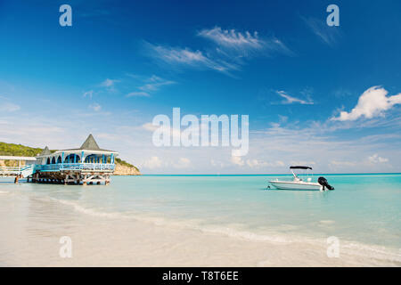 Godetevi i vantaggi di essere accanto al mare. Mare turchese bungalow sull'acqua e nave vicino alla spiaggia. Vacanza mare spiaggia di sabbia casa tropicale bungalow.st Johns Antigua. Idilliaco giorno di sole in riva al mare a cielo blu. Foto Stock