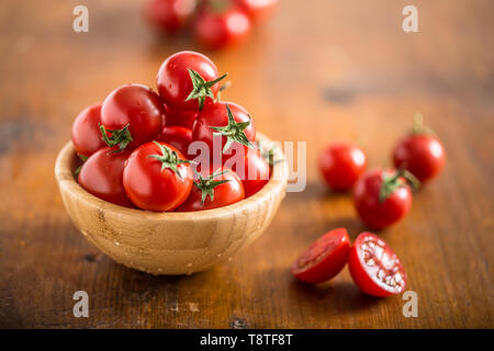 Freschi pomodori ciliegia in ciotola di legno su un tavolo di legno Foto Stock