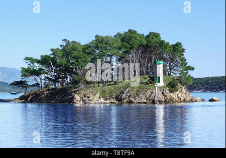 La riflessione di piccolo faro nel bel mare blu superficie nella parte anteriore del porto della città di Rab sul litorale croato, circondato da antichi verde pino Foto Stock