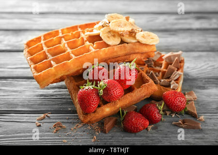 Deliziosi waffles con banana, frutti di bosco e cioccolato su sfondo di legno Foto Stock