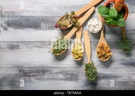 Cucchiai con diverse erbe e pillole sul tavolo di legno Foto Stock