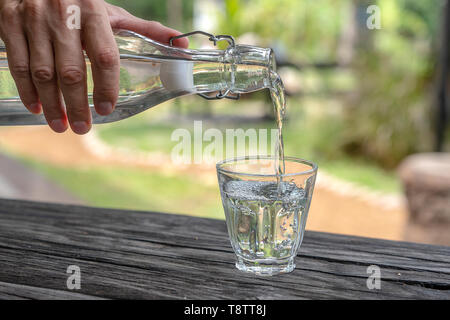 Un cameriere in un ristorante si versa acqua fresca da una bottiglia in un bicchiere, vicino all'aperto Foto Stock