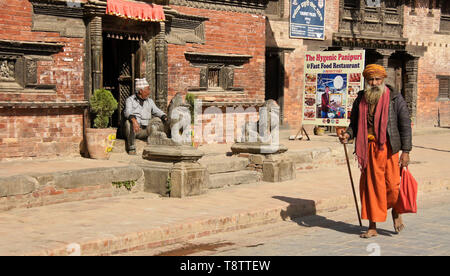 Un sadhu indù (uomo santo) passeggiate passato vecchi edifici in mattoni su Durbar Square, Patan, Valle di Kathmandu, Nepal Foto Stock