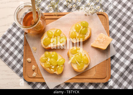 Gustosi panini con formaggio, uva e miele sul pannello di legno Foto Stock