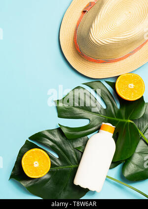 Estate cappello di paglia sunscreen foglia verde di un esotico monstera impianto luminoso sfondo blu. Il concetto di vacanze estive Foto Stock