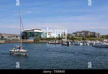 Yacht vele fuori da Sutton Harbour Plymouth con National Marine Aquarium e marina in background Foto Stock