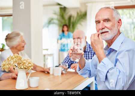 Senior l uomo si prende tablet con un sorso di acqua presso la casa di riposo Foto Stock