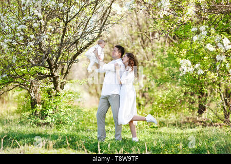 La famiglia felice sul giardino di primavera. Mamma, papà e bimbo piccolo figlia sono a piedi nella fioritura cespugli di ciliegio in primavera Foto Stock