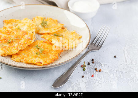 Hommade frittelle di patate - röstinchen, hash browns, kartoffelpuffer, latkes, draniki - con sourcream su sfondo grigio Foto Stock