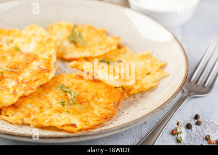 Hommade frittelle di patate - röstinchen, hash browns, kartoffelpuffer, latkes, draniki - con sourcream su sfondo grigio Foto Stock