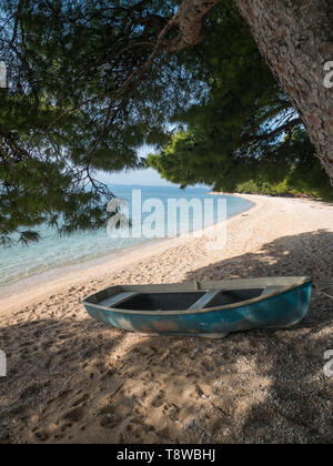 Piccola barca sulla spiaggia sotto gli alberi di pino in Tucepi, Croazia Foto Stock