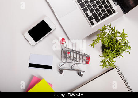 Shopping online. Carta bancaria nelle vicinanze di un laptop e mini carrello su sfondo bianco vista dall'alto. Foto Stock