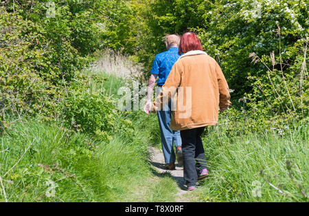 Coppia senior di persone a piedi lungo un sentiero di campagna in primavera nel West Sussex, in Inghilterra, Regno Unito. Foto Stock