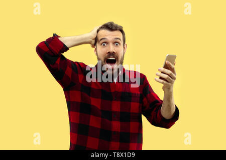 A mezza lunghezza close up ritratto di Giovane Uomo in camicia su sfondo giallo. Le emozioni umane, espressione facciale concetto. Vista frontale. Colori alla moda. Lo spazio negativo. Un delirio di notizie in smartphone. Foto Stock