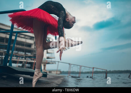 La ballerina sta ballando sulla costa del fiume in un nero e rosso tutu sullo sfondo dell'edificio. Foto Stock