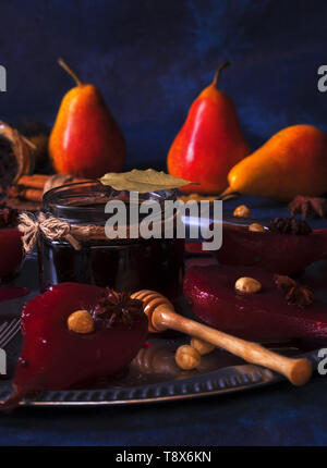 Hibiscus pere in camicia, dolce dessert di frutta. Vassoio in argento con pere, abbellito con nocciole, foglie di alloro, essiccati Fiori di ibisco, anice stelle, e Foto Stock