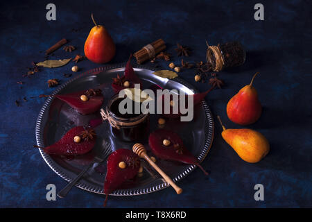 Hibiscus pere in camicia, dolce dessert di frutta. Vassoio in argento con pere, abbellito con nocciole, foglie di alloro, essiccati Fiori di ibisco, anice stelle, e Foto Stock