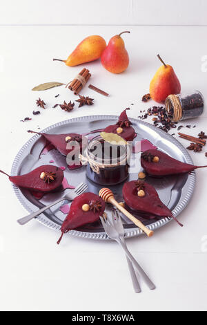 Hibiscus pere in camicia, dolce dessert di frutta. Vassoio in argento con pere, abbellito con nocciole, foglie di alloro, essiccati Fiori di ibisco, anice stelle, e Foto Stock