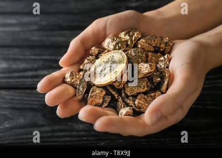 Mani femminili di pepite d'oro e bitcoin scuro su sfondo di legno Foto Stock