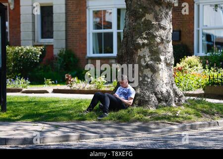 Tenterden, Kent, Regno Unito. 15 Maggio, 2019. Regno Unito: Meteo Bella giornata di sole a Tenterden high street come la gente camminare intorno al centro città godere del bel tempo caldo. Un giovane uomo si siede in ombra sotto un albero. Credito: Paolo Lawrenson/Alamy Live News Foto Stock