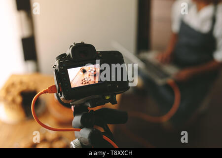 La donna la registrazione di video in cucina durante la preparazione di paste dolci, focus sul display della fotocamera. Pastry chef rendendo un videoblog in cucina. Foto Stock