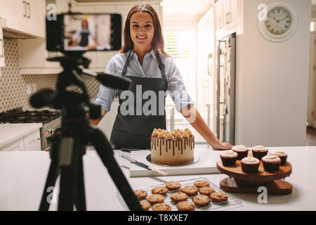 La donna la registrazione di video in casa sua cucina. Pastry chef creare contenuti per blog video. Foto Stock