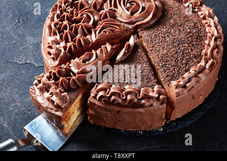 Close-up di una meringa al cioccolato torta festosa e rabboccato con la crema di burro al cioccolato e rose commestibili argento confetto tagliato a fettine su una piastra su un calcestruzzo Foto Stock