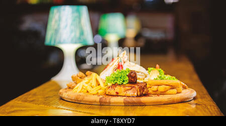 Pub menu snack. Ad alto contenuto calorico snack per il gruppo amici. Gustosi spuntini deliziosi. Snack per la birra. Il cibo del ristorante. Tavola di legno con un sacco di patatine fritte bastoncini di pesce burrito e bistecca di carne con insalata mista. Foto Stock