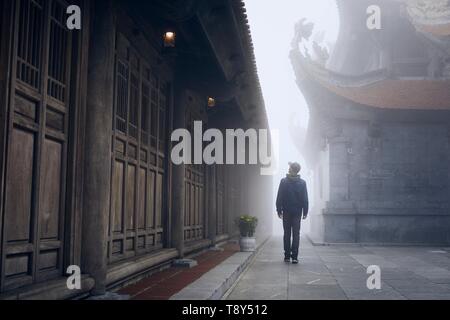 Viaggiatore a piedi nella misteriosa nebbia al tempio buddista sul picco Fansipan - montagna più alta in Indocina, Vietnam. Foto Stock