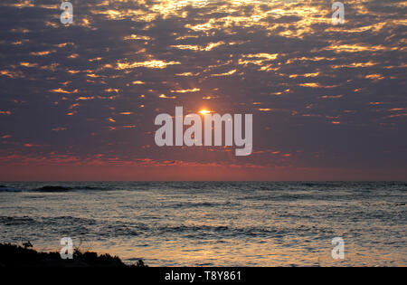 Sembra oro liquido se le incrinature nelle nuvole e con il sole arancione spiata attraverso uno troppo, con l'Oceano Atlantico in primo piano. Foto Stock