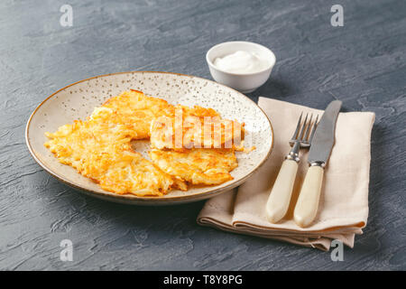 Hommade frittelle di patate - röstinchen, hash browns, kartoffelpuffer, latkes, draniki - con sourcream su sfondo grigio Foto Stock