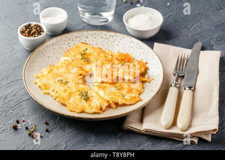 Hommade frittelle di patate - röstinchen, hash browns, kartoffelpuffer, latkes, draniki - con sourcream su sfondo grigio Foto Stock