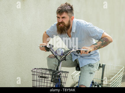 Hipster con bracci tatuati guidare la bicicletta. Uomo Barbuto viaggiare in bici il trasporto. Moda Uomo con barba lunga in jeans strappati e camicia. Per viaggiare o Foto Stock