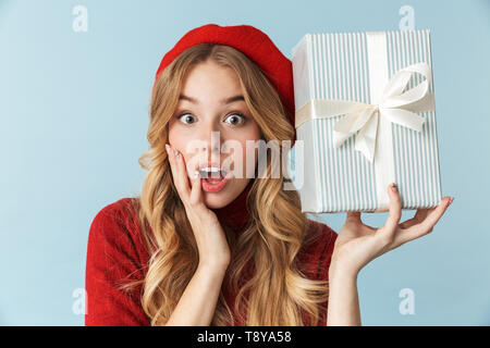 Immagine di donna affascinante 20s indossando berretto rosso azienda confezione regalo isolate su sfondo blu in studio Foto Stock