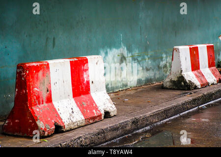 Rosso Bianco concret arresto barriera andando segno sulla strada attuale sul sentiero verde verniciato vecchio muro sfondo Foto Stock