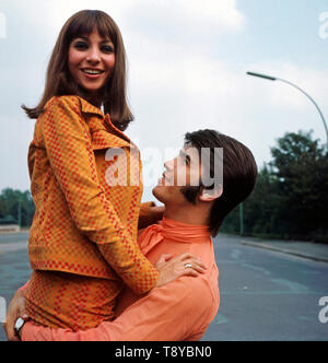 Das Musikerpaar israelische Esther & Abi Ofarim posiert in orangefarbener Kleidung auf der Hauptstraße welche vom Brandenburger Tor wegführt und Westdeutschland von Ostdeutschland trennt, Deutschland 1967. Il musicista israeliano giovane Esther & Abi Ofarim in posa di vestiti arancioni sulla strada principale che conduce lontano dalla Porta di Brandeburgo e separa la Germania Ovest dalla Germania orientale, Germania 1967. Foto Stock